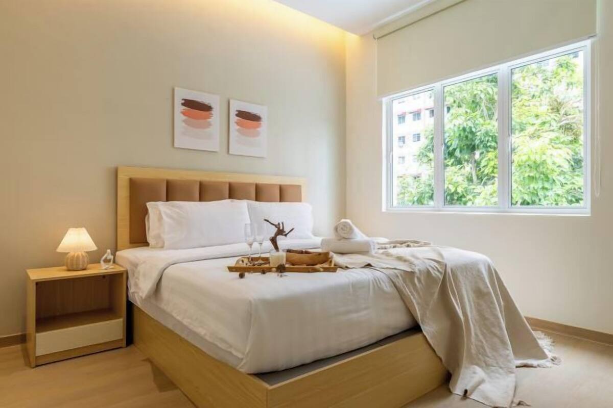 A bedroom with a bed, bedside table, lamp, artwork, and a window with a view.