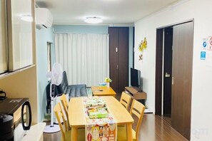 A dining area with a table set for four, a fan, a television, and a door with a sign. - Yodogawa Flower Private Accommodation (Osaka)