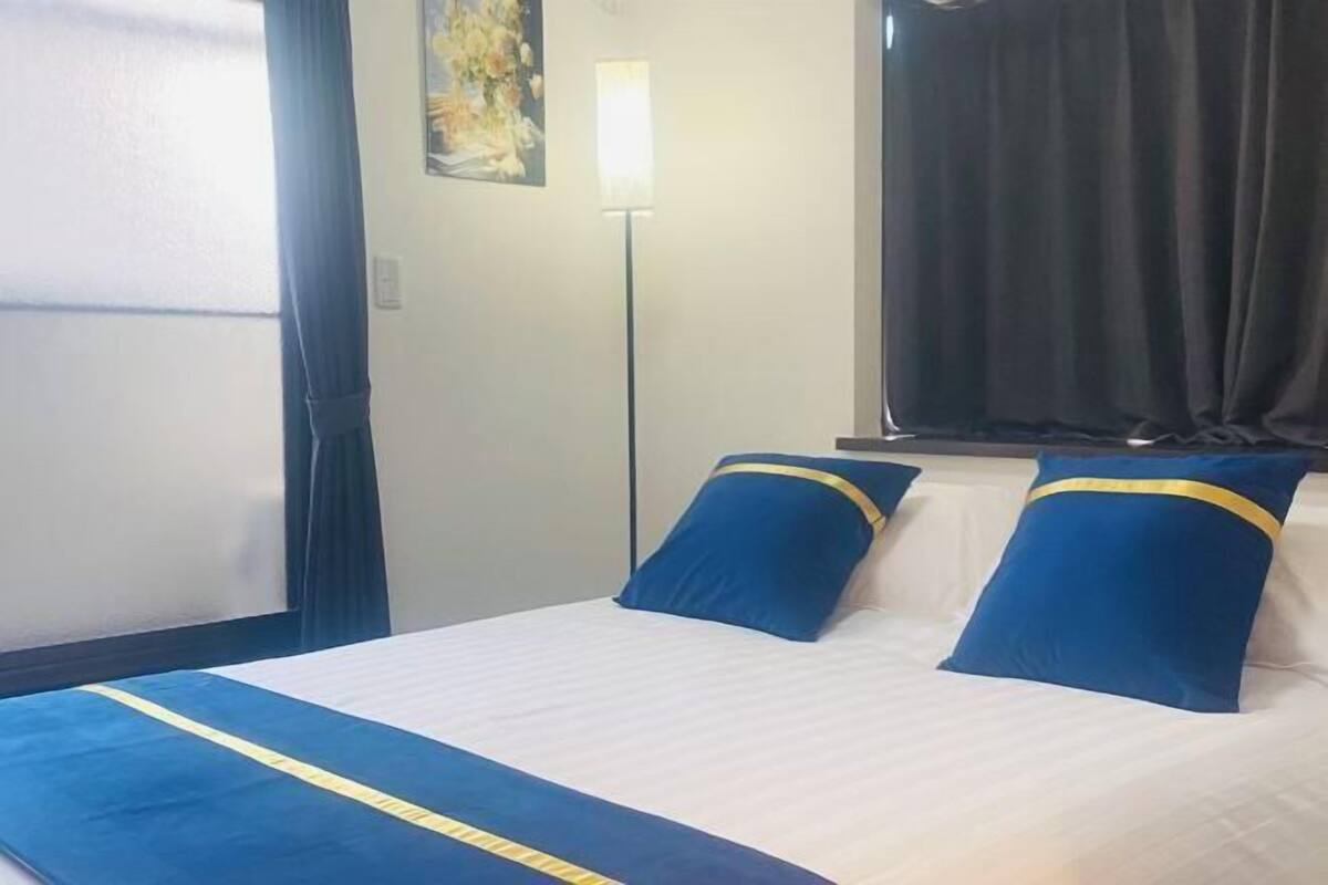 Una habitación de hotel con cama, mesita de noche, lámpara y ventana con cortinas.