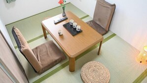 A tatami mat room with a wooden table, two chairs, a small woven stool, a vase with flowers, and a remote control on the table. - Yodogawa Flower Private Accommodation (Osaka)
