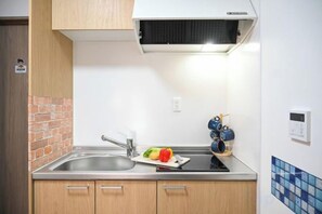 Una cocina con un fregadero, una estufa y un horno empotrado. Hay armarios debajo de la encimera y un ventanal pequeño sobre el fregadero.