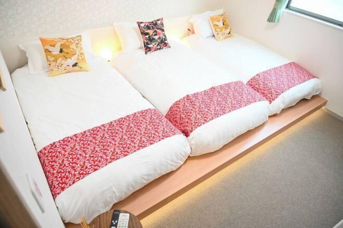 Una cama doble con ropa de cama blanca y roja, una mesita de noche y una ventana con cortinas.