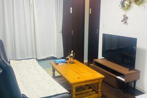 A living room with a sofa, a wooden coffee table, a TV on a stand, and a wardrobe. - Yodogawa Flower Private Accommodation (Osaka)