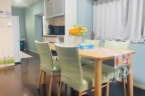 A dining area with a wooden table, green upholstered chairs, a vase with flowers, and a patterned table runner. - Yodogawa Flower Private Accommodation (Osaka)