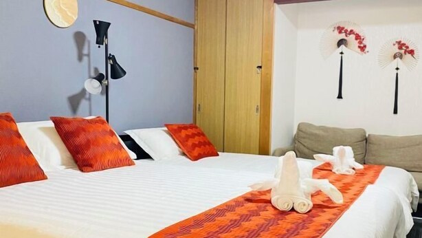 A hotel room with a bed, pillows, a bedside lamp, a wardrobe, and decorative fans. - Yodogawa Flower Private Accommodation (Osaka)