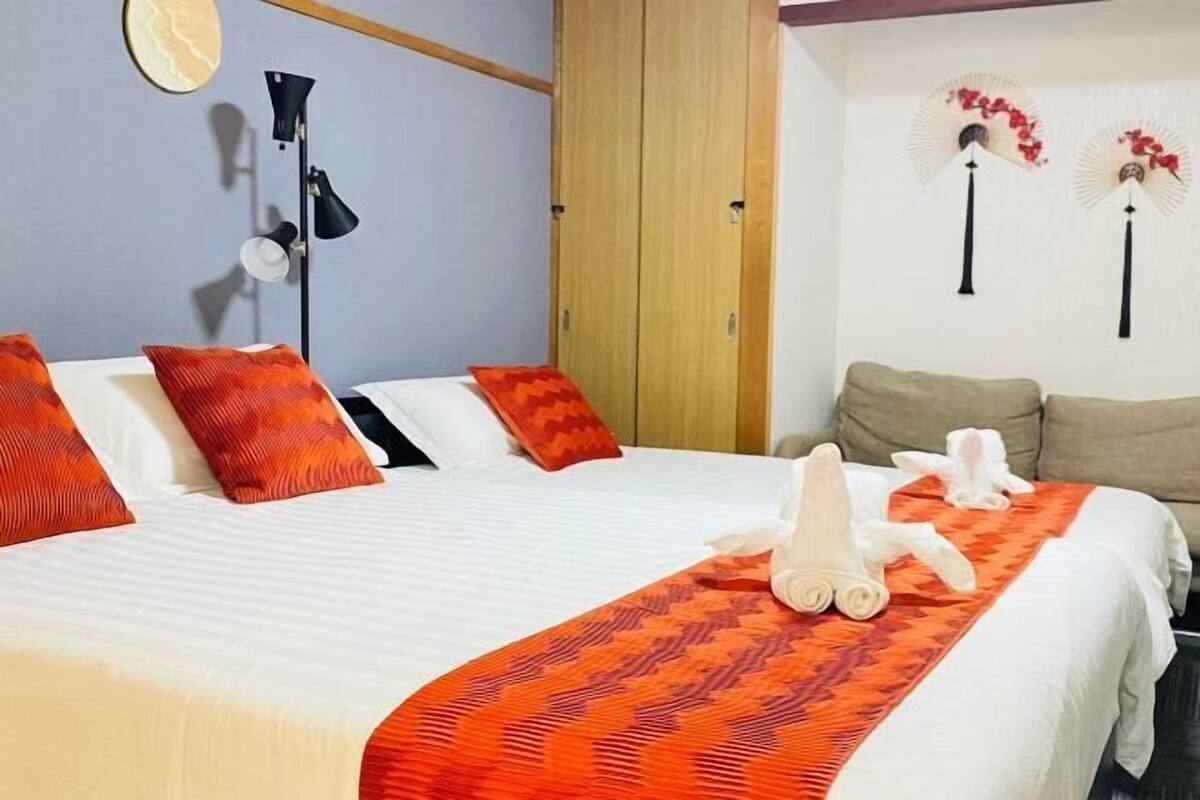 Habitación de hotel con cama, almohadas, lámpara de noche, armario y adornos con motivos de abanicos.