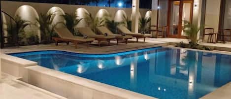 An outdoor swimming pool with lounge chairs and palm trees.