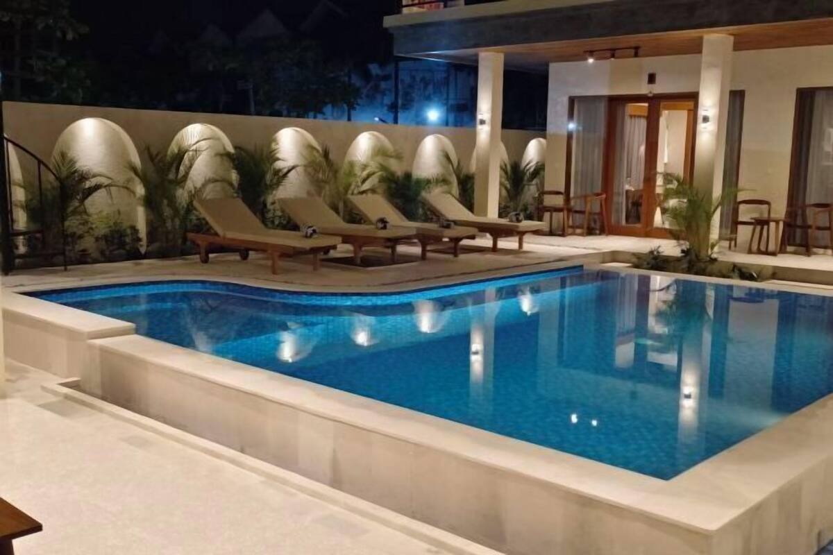 A swimming pool with lounge chairs, a covered seating area, and a building with columns.