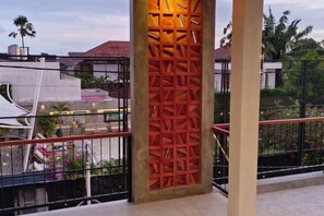 A balcony with a metal railing, a decorative red lattice structure, and a view of a building with a red roof. - Fullmoon Canggu Nelayan (Bali)
