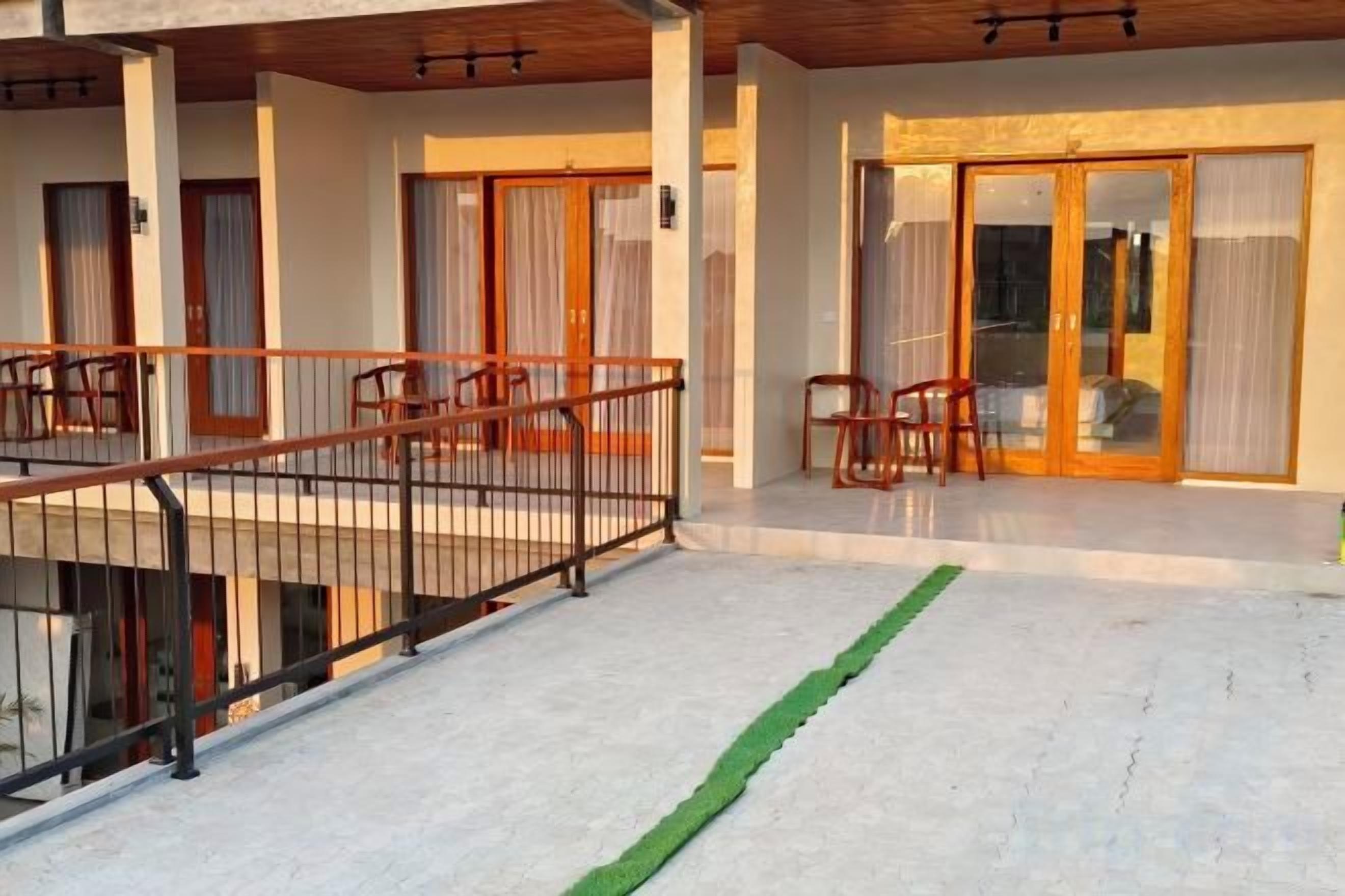 A hotel exterior with a covered outdoor seating area, a staircase, and a glass door entrance.