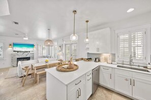Une cuisine moderne avec des meubles blancs, un îlot central doté d’un plan de travail en marbre et des luminaires suspendus.