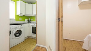 A compact kitchen with a washing machine, a coffee maker, and a stove. - Glenville Apartment (Greater London)