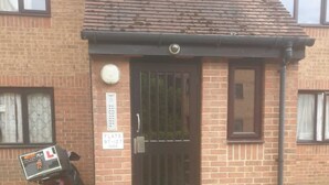 A brick building with a black door, a small porch, and a motorcycle parked outside. - Glenville Apartment (Greater London)