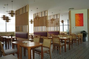 A restaurant with wooden furniture, cushioned seating, and pendant lighting. - Signature Beach at The Arena Cam Ranh (Cam Ranh)