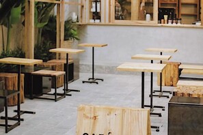 Interior de una cafetería con varias mesas y sillas de madera, algunas con patas metálicas.
