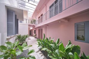 Un estrecho pasillo interior con pared rosa, plantas en macetas y techo de vidrio.