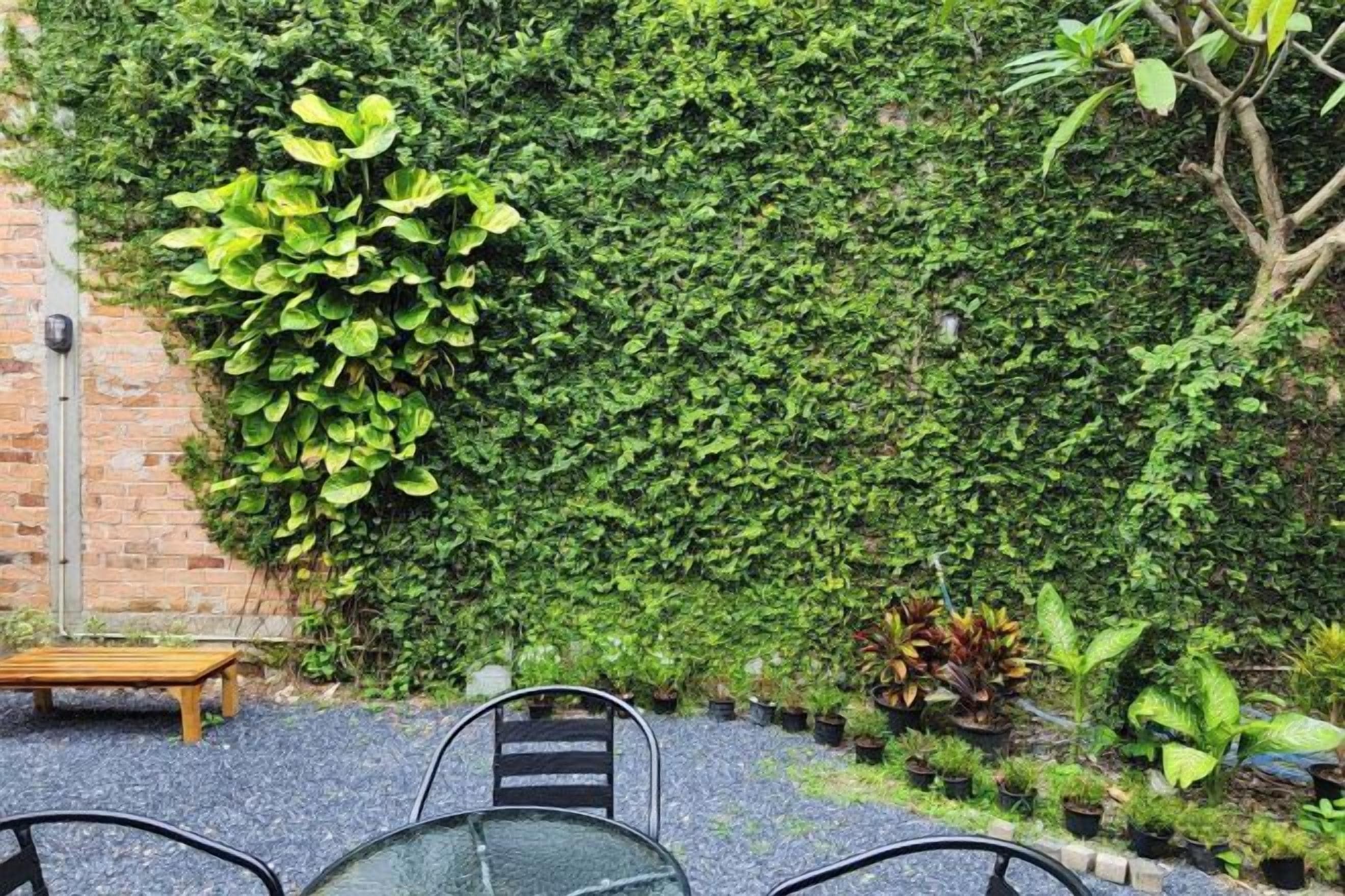 An outdoor seating area with a brick wall covered in greenery, a wooden bench, and a table with chairs.
