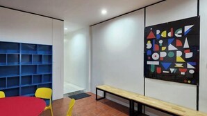 A modern interior with a red table, yellow chairs, a wooden bench, and a colorful abstract art piece on the wall. - RYB Hostel Phuket (Phuket)