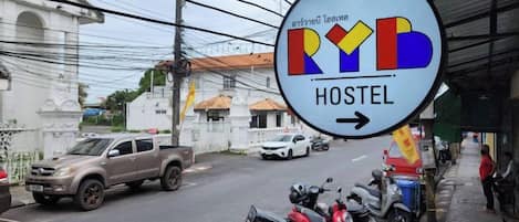 Señal de un albergue con una flecha direccional, motocicletas estacionadas y vista de la calle con edificios.