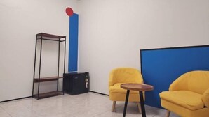 A room with a blue accent wall, a yellow armchair, a wooden side table, and a metal shelving unit. - RYB Hostel Phuket (Phuket)