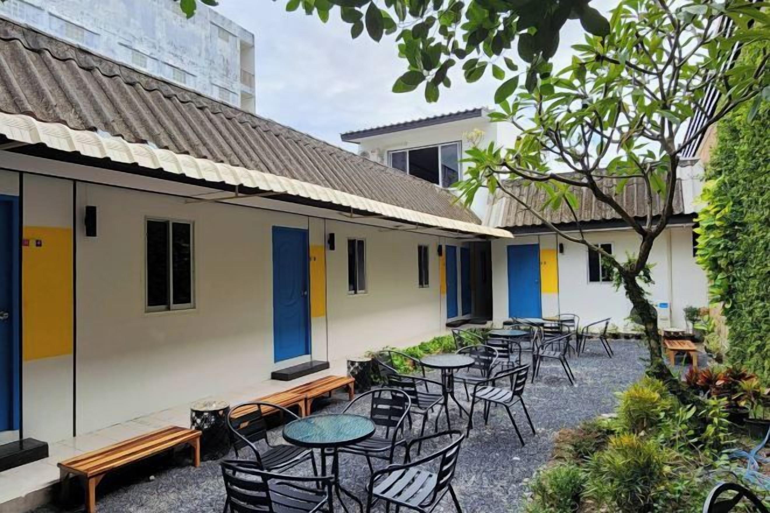 Un patio con mesas al aire libre, un edificio con puertas azules y un árbol.