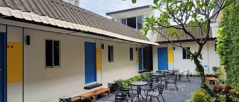 A courtyard with outdoor seating, a building with blue doors, and a tree.