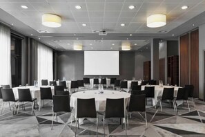 A conference room with round tables, chairs, a projector screen, and a large window. - Courtyard by Marriott Munich City East (Munich)