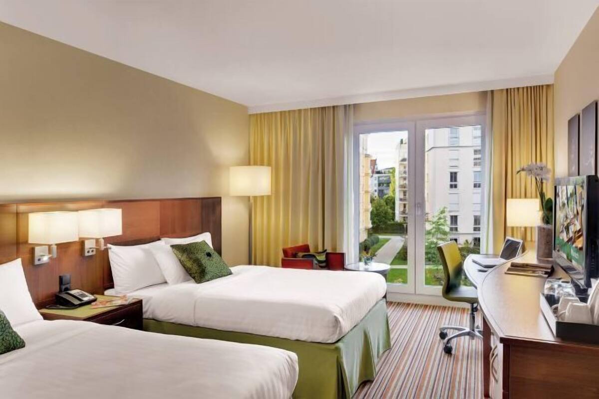 A hotel room with two beds, a desk with a computer, a TV, and a view of the city.