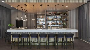 A modern bar area with a long counter, multiple hanging pendant lights, and a variety of bottles on shelves. - Courtyard by Marriott Munich City East (Munich)
