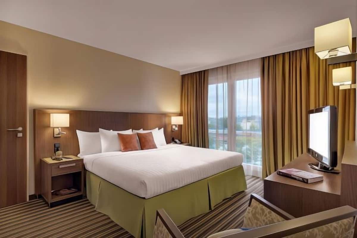 A hotel room with a large bed, two bedside lamps, a TV, and a view of the outdoors.