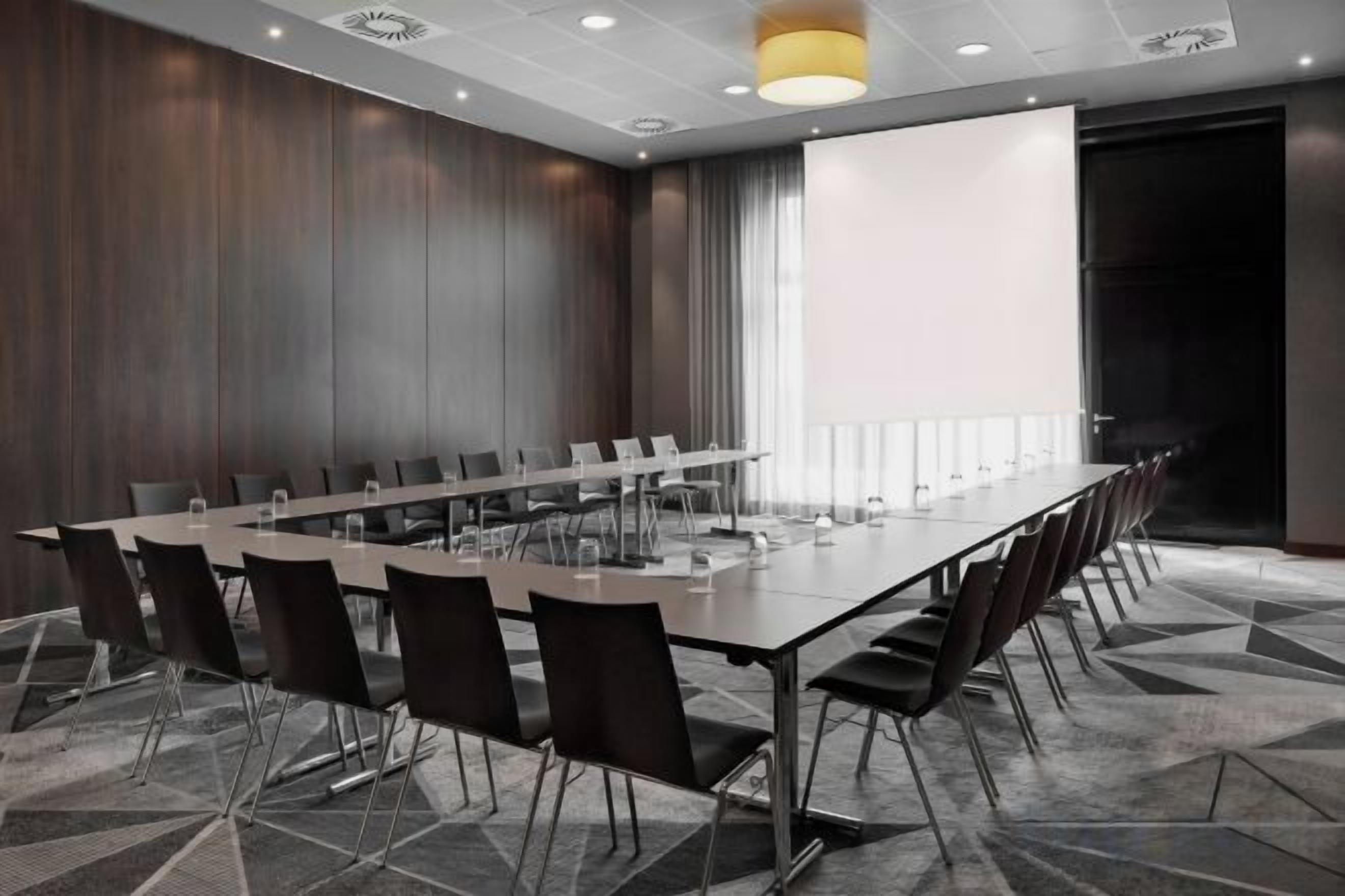 A conference room with a long table, chairs, a projector screen, and a carpeted floor.