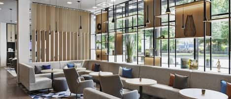 A modern lounge area with seating arrangements, large windows, and pendant lighting.