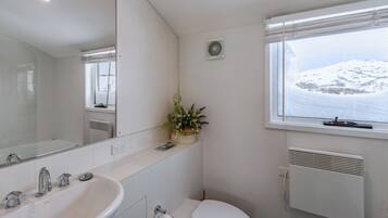 A bathroom with a white sink, a toilet, a mirror, and a window with a view of a snowy landscape.
