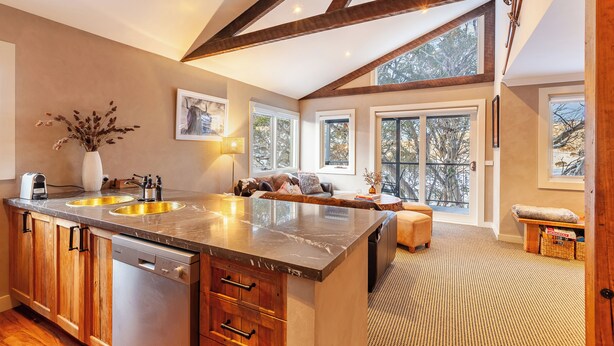 A spacious kitchen with a large island, wooden cabinets, and a view of the outdoors through large windows. - The Stables Resort Perisher - Open All Year (Perisher Valley)