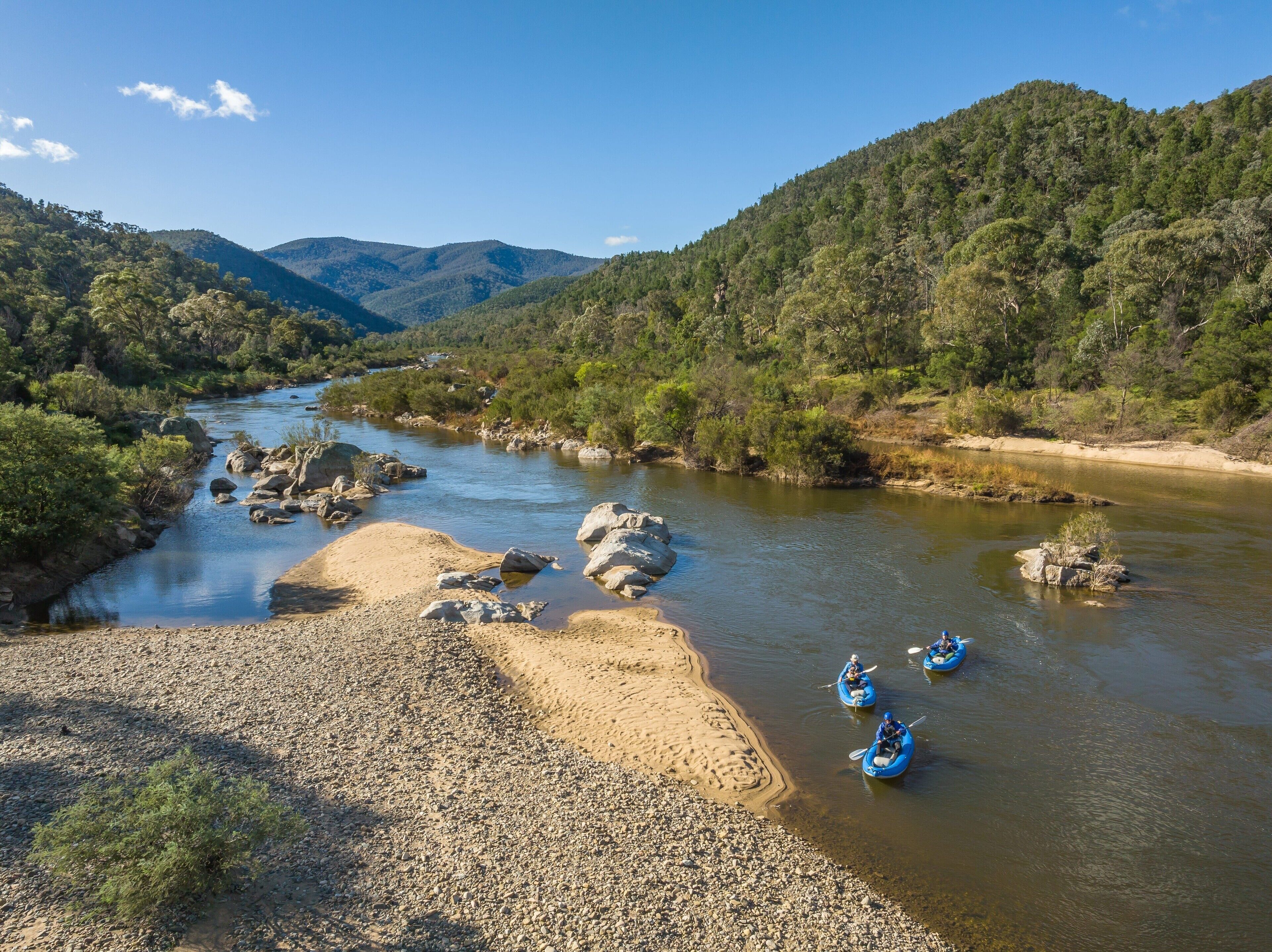 A river with kayaks, surrounded by hills and trees.