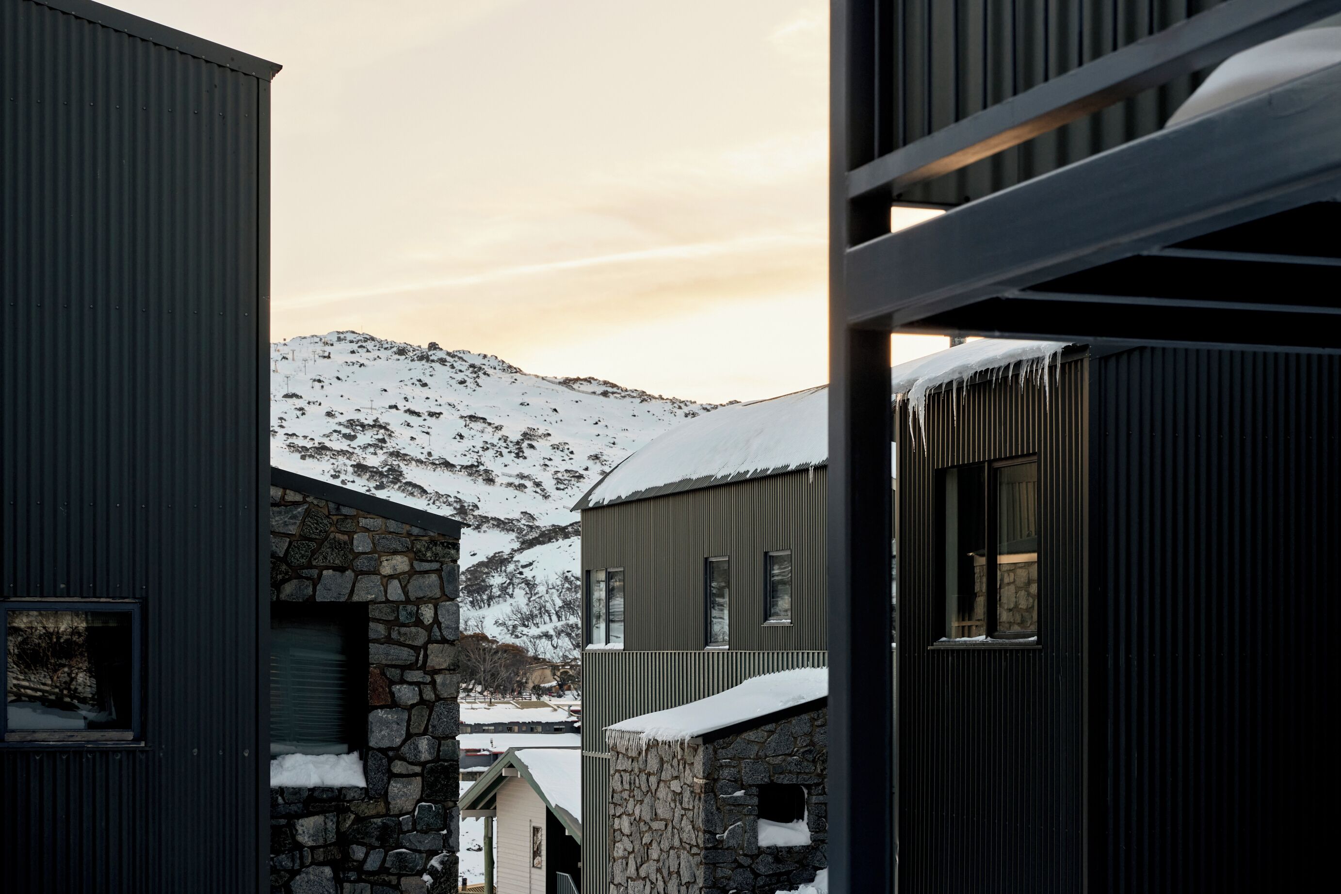Un bâtiment moderne doté d’une façade en pierre et d’une structure extérieure en métal, avec de nombreuses fenêtres et une vue sur des montagnes enneigées en arrière-plan.
