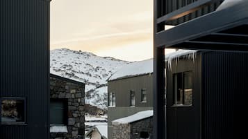 Un bâtiment moderne doté d’une façade en pierre et d’une structure extérieure en métal, avec de nombreuses fenêtres et une vue sur des montagnes enneigées en arrière-plan.