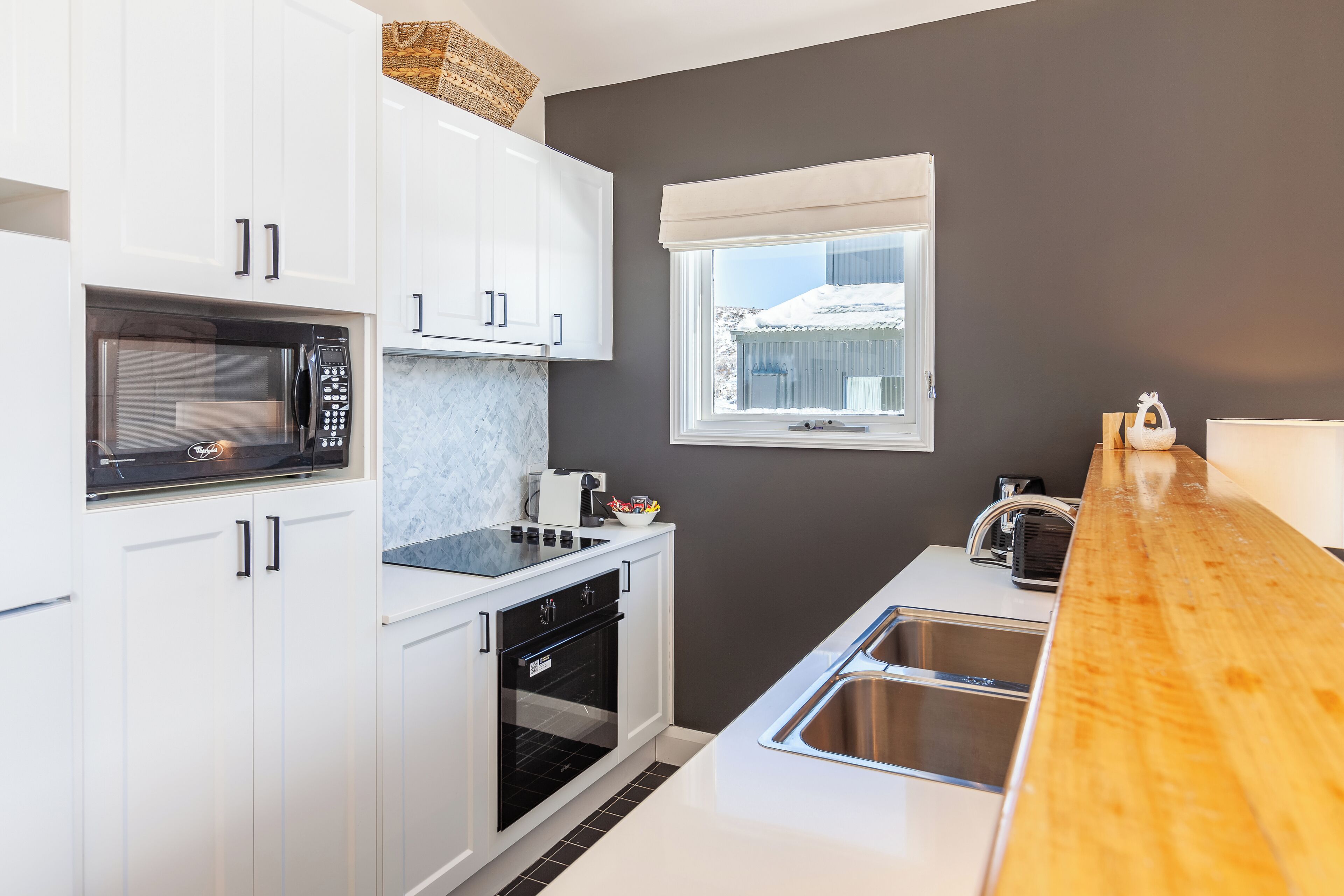 A modern kitchen with white cabinets, a microwave, an oven, and a wooden countertop.