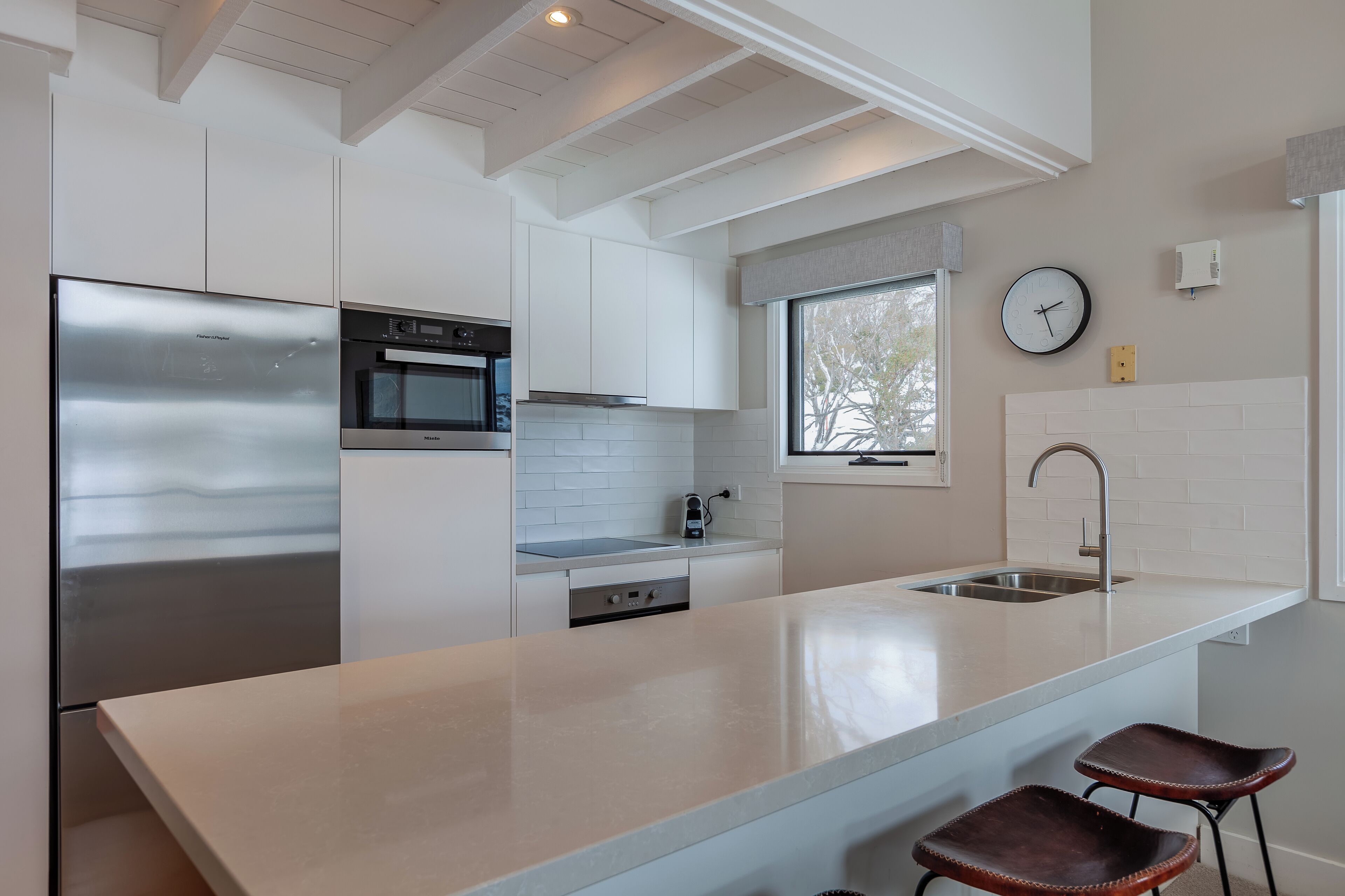 A modern kitchen with a stainless steel refrigerator, a built-in oven, and a large island with bar stools.