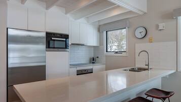A modern kitchen with a stainless steel refrigerator, a built-in oven, and a large island with bar stools.