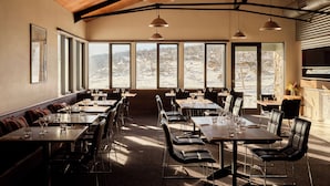 A restaurant with large windows offering a view of a snowy landscape. Tables and chairs are arranged for dining. - The Stables Resort Perisher - Open All Year (Perisher Valley)