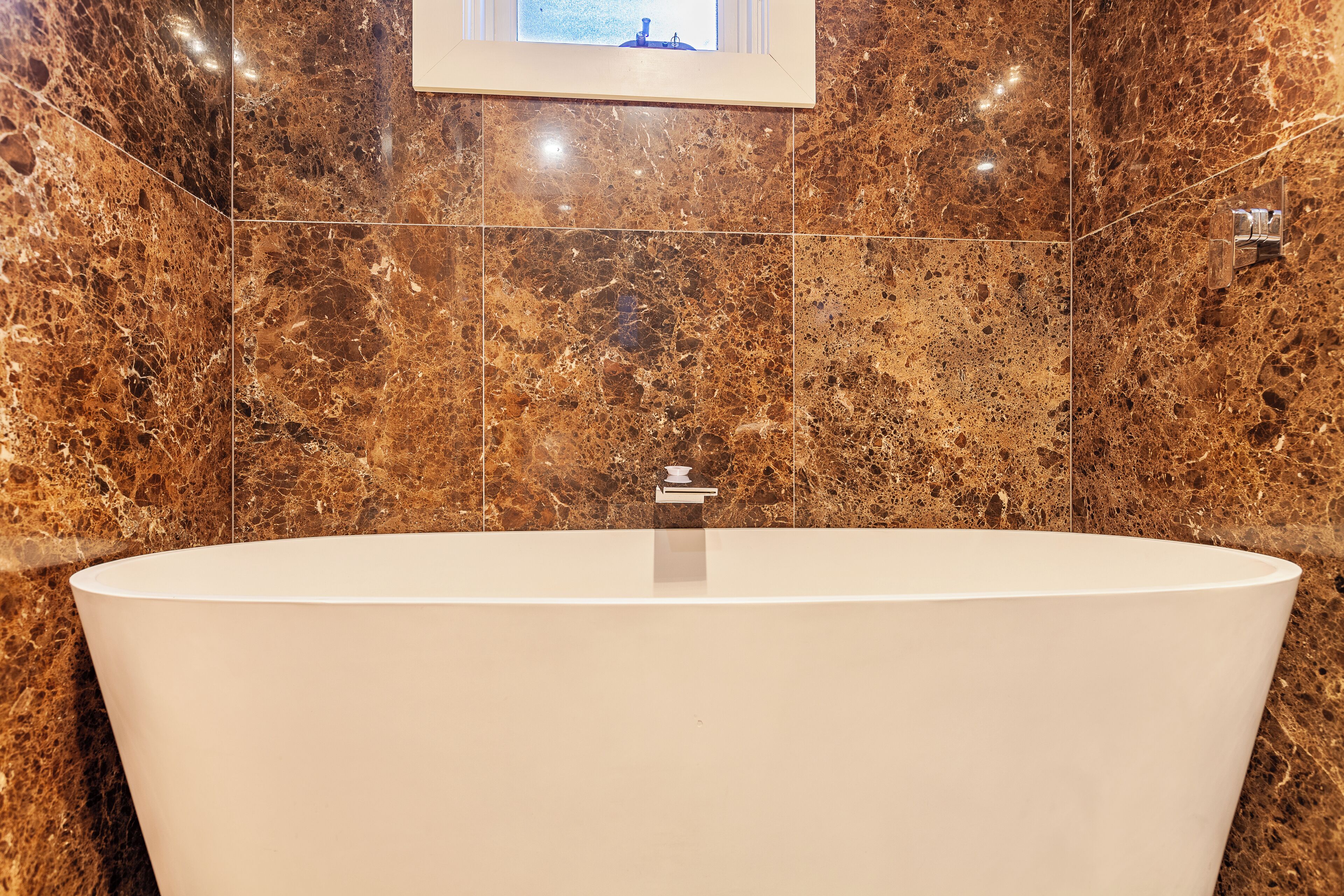 Ein modernes Badezimmer mit einer freistehenden Badewanne, Marmorwänden und einem gerahmten Bild über der Wanne.