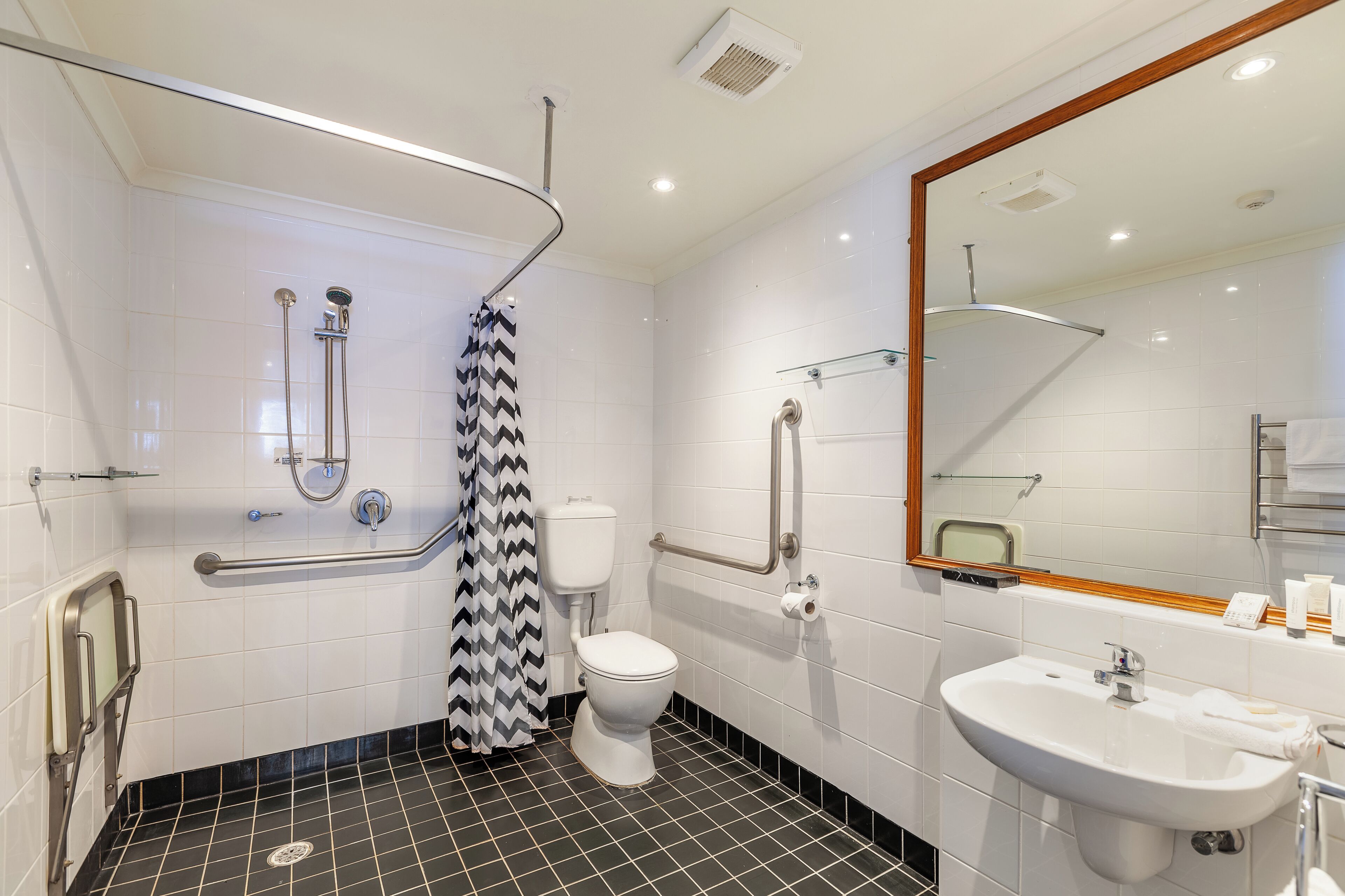 A modern bathroom with a black and white tiled floor, a white toilet, a sink, and a shower area with a black and white patterned shower curtain.