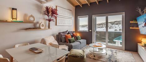 Una sala de estar moderna con una mesa blanca, un sofá gris y un amplio ventanal con vistas nevadas.