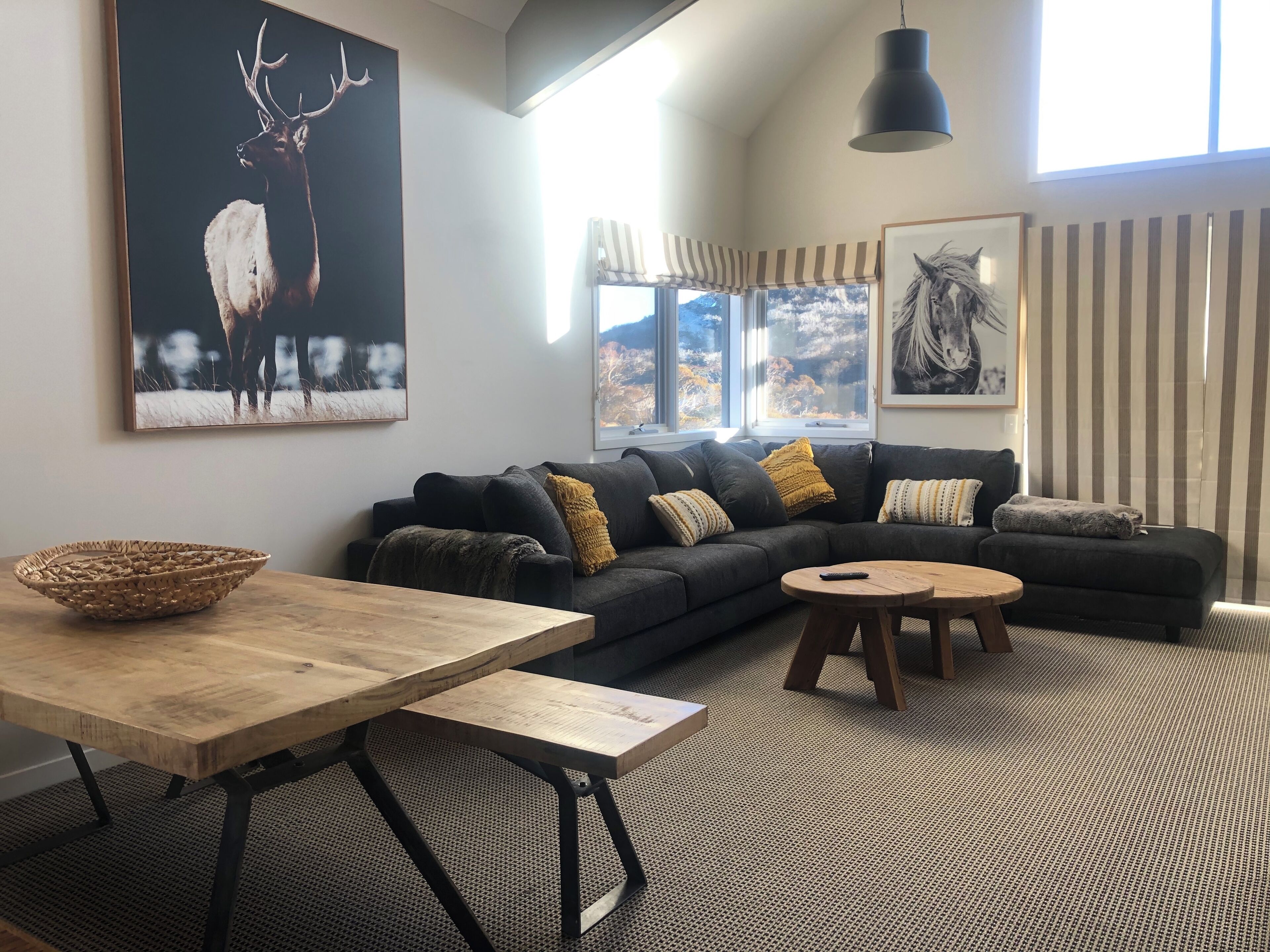 A modern living room with a dark grey sectional sofa, a wooden coffee table, a woven side table, and a large framed deer painting.