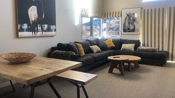 A modern living room with a dark grey sectional sofa, a wooden coffee table, a woven side table, and a large framed deer painting.