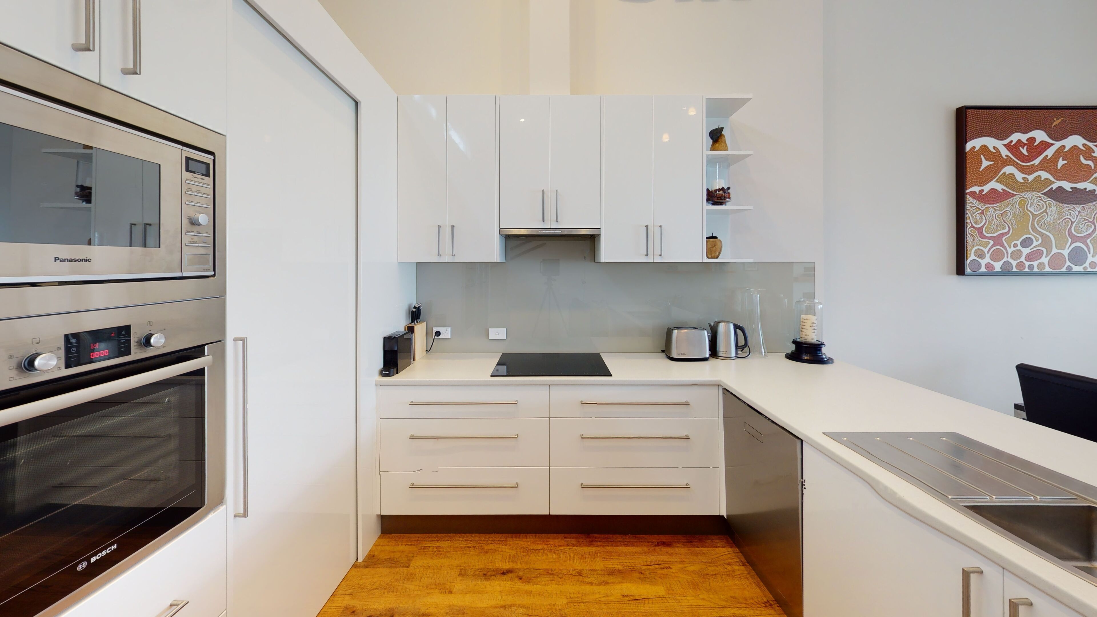 A compact kitchen with white cabinets, a Bosch oven, a microwave, and a sink.