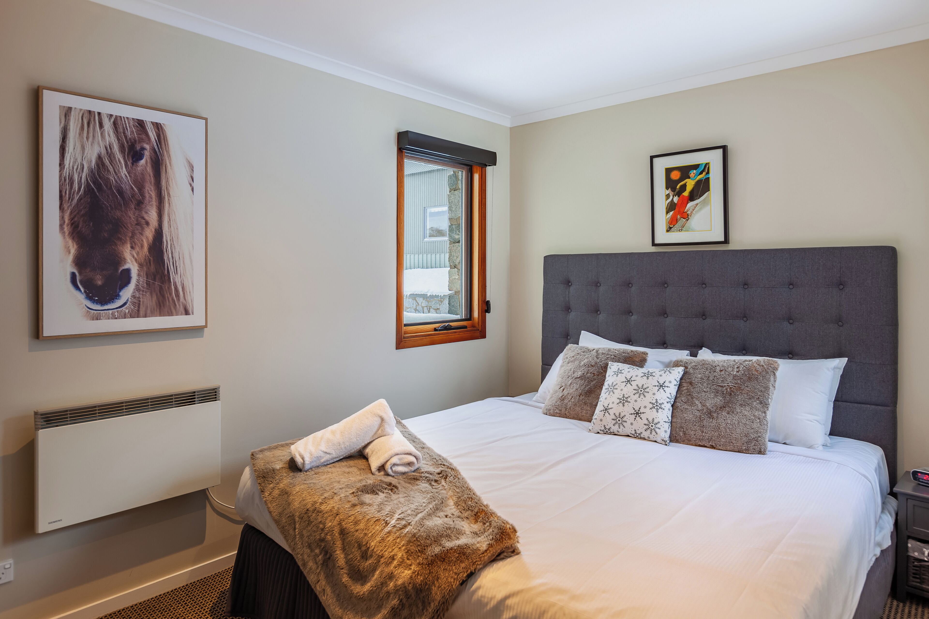 A bedroom with a large bed, a window, a radiator, and artwork on the walls.