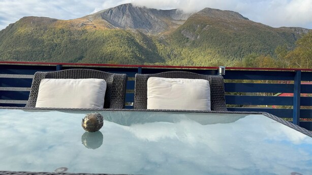 A glass-top table with wicker chairs and cushions, overlooking a mountainous landscape. - Spacious house, with boat, in beautiful landscape (Tustna)