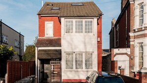 A two-story house with a garage, a car parked in front, and a red brick facade. - 1 Bed Flat Wanstead E11 2PF | Save 10% LongStay | Contractors | Wi-Fi | Sleeps4 | Parking (Greater London)